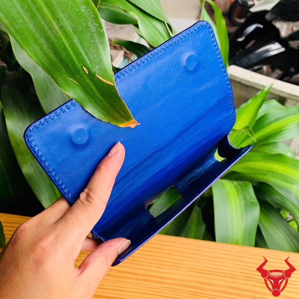 Bao Da Đeo Thắt Lưng Da Bụng Cá Sấu Xanh Navy OFAA8 – Cao Cấp Thượng Hạng Bao da đeo thắt lưng da bụng cá sấu màu xanh navy OFAA8, cầm trên tay, nền lá xanh, logo đỏ góc phải.