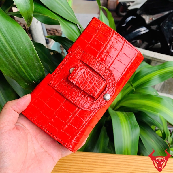 Bao Da Đeo Thắt Lưng Da Cá Sấu Màu Đỏ OFAA8 – Đẳng Cấp Sang Trọng Bao da đeo thắt lưng da cá sấu màu đỏ OFAA8, cầm trên tay, nền lá xanh, logo đỏ góc phải.
