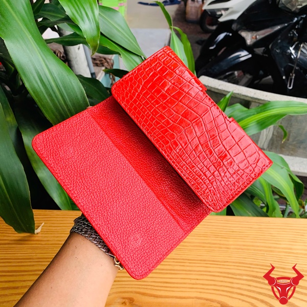 Bao Da Đeo Thắt Lưng Da Cá Sấu OFAA8 – Sang Trọng Và Đẳng Cấp Bao da đeo thắt lưng da cá sấu màu đỏ OFAA8, cầm trên tay, nền lá xanh, logo đỏ góc phải.