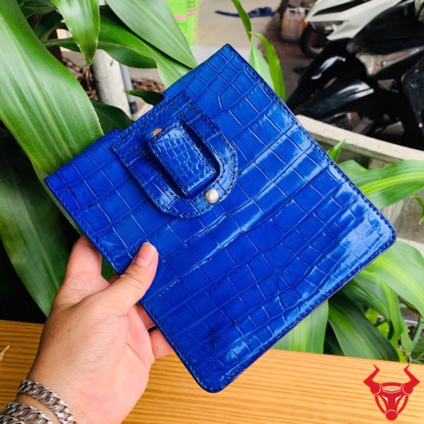 Bao Da Đeo Thắt Lưng Da Cá Sấu OFAA8 – Sang Trọng Cao Cấp Quý Ông Bao da đeo thắt lưng da cá sấu màu xanh dương OFAA8, cầm trên tay, nền lá xanh, logo đỏ góc phải.