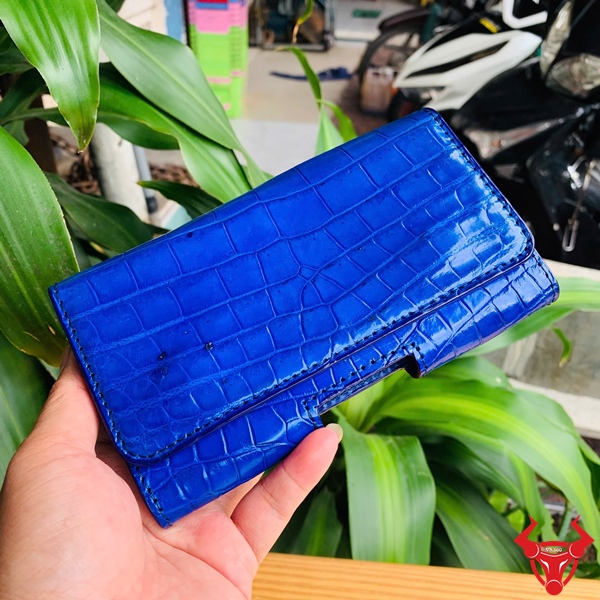 Bao Da Đeo Thắt Lưng Da Cá Sấu Màu Xanh Dương OFAA8 – Cao Cấp Sang Trọng Bao da đeo thắt lưng da cá sấu màu xanh dương OFAA8, cầm trên tay, nền lá xanh, logo đỏ góc phải.