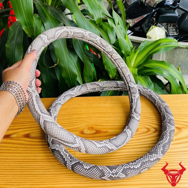 Phong Cách Cao Cấp Cho Tài Xế Bọc vô lăng da trăn màu xám trắng họa tiết trăn, đường kính 33cm, đặt trên bàn gỗ, logo đỏ góc phải.