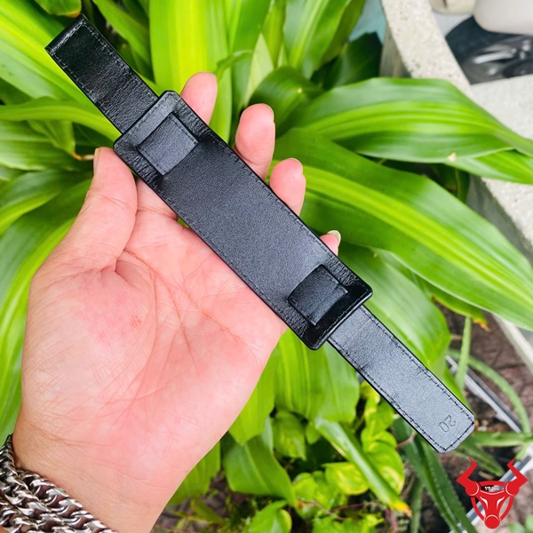 Dây Đồng Hồ Da Kèm Đệm Mặt Size 20 Dây đồng hồ da kèm đệm mặt size 20, màu đen, cầm trên tay, nền lá xanh, logo đỏ góc phải.