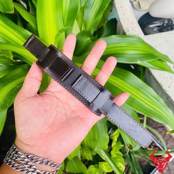 Dây Đồng Hồ Da Kèm Đệm Mặt Size 20 Dây đồng hồ da kèm đệm mặt size 20, màu đen, cầm trên tay, nền lá xanh, logo đỏ góc phải.