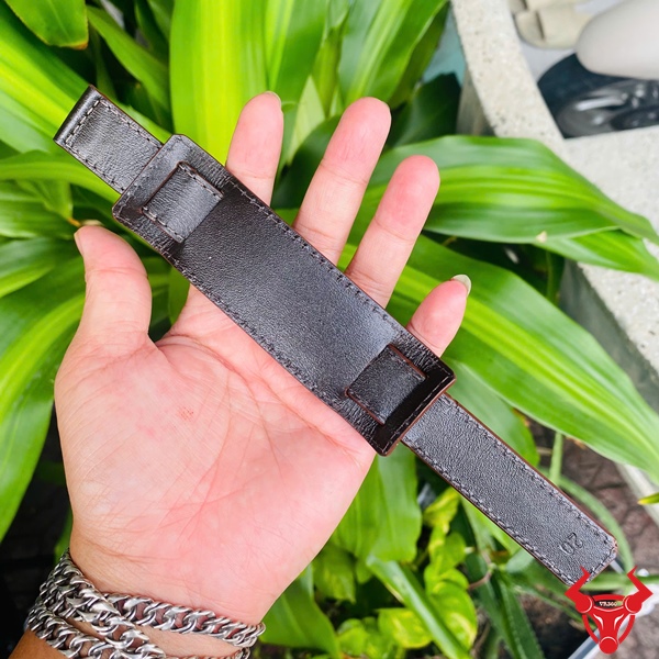 Dây Đồng Hồ Da Kèm Đệm Mặt Size 20 Dây đồng hồ da kèm đệm mặt size 20, màu đen, cầm trên tay, nền lá xanh, logo đỏ góc phải.