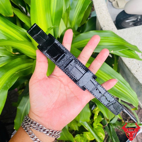 Dây Đồng Hồ Da Kèm Đệm Mặt Size 20 Dây đồng hồ da kèm đệm mặt size 20, màu đen, cầm trên tay, nền lá xanh, logo đỏ góc phải.
