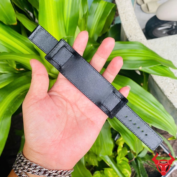 Dây Đồng Hồ Da Kèm Đệm Mặt Size 20 Dây đồng hồ da kèm đệm mặt size 20, màu đen, cầm trên tay, nền lá xanh, logo đỏ góc phải.