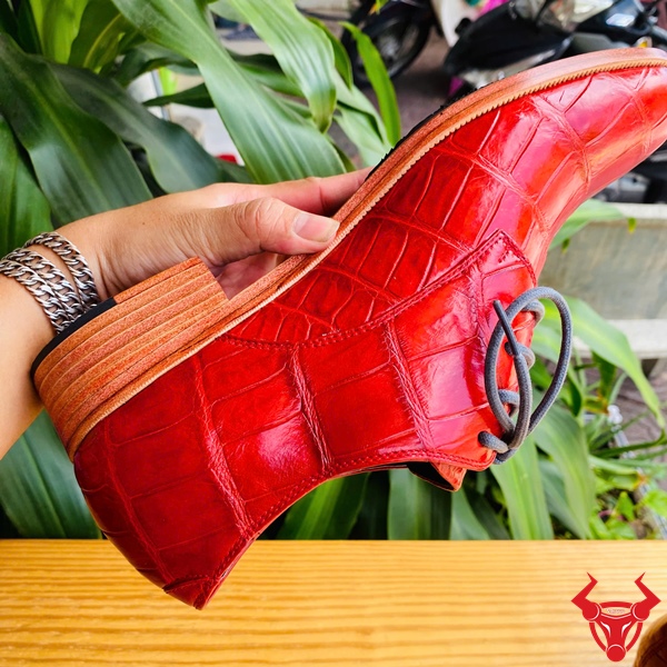 Giày Tây Đóng Thủ Công Da Bụng Cá Sấu GAA8 – Cá Tính Cao Cấp Thời Thượng Giày tây đóng thủ công da bụng cá sấu GAA8 màu đỏ, dây buộc xám, đặt trên bàn gỗ, nền lá xanh, logo đỏ góc phải.