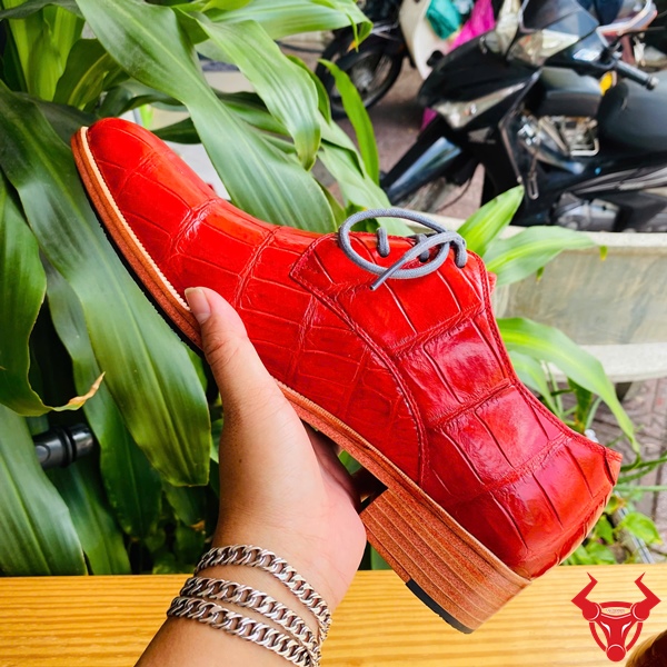 Giày Tây Da Cá Sấu GAA8 – Đẳng Cấp Thời Thượng Cho Bạn Giày tây đóng thủ công da bụng cá sấu GAA8 màu đỏ, dây buộc xám, đặt trên bàn gỗ, nền lá xanh, logo đỏ góc phải.
