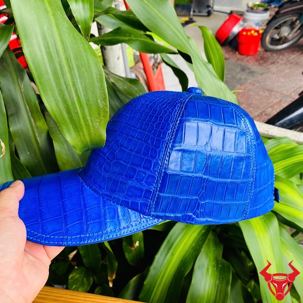 Mũ NOA8 Xanh Dương Cao Cấp Đầy Cá Tính Mũ lưỡi trai xanh dương da cá sấu trên bàn gỗ, tay cầm, nền cây xanh mát.
