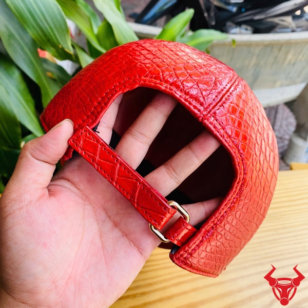 Mũ Lưỡi Trai Da Cá Sấu NOA8 – Đẳng Cấp Thời Thượng Cho Bạn Mũ lưỡi trai da bụng cá sấu NOA8 màu đỏ, đặt trên bàn gỗ, nền lá xanh, logo đỏ góc phải.