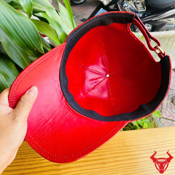 Mũ Lưỡi Trai Da Bụng Cá Sấu NOA8 – Phong Cách Cao Cấp Độc Đáo Mũ lưỡi trai da bụng cá sấu NOA8 màu đỏ, đặt trên bàn gỗ, nền lá xanh, logo đỏ góc phải.
