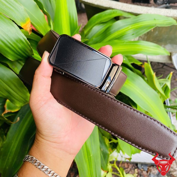 TLRN17 – Thắt Lưng Da Bò Thật Bền Bỉ Và Thanh Lịch Thắt lưng da bò màu nâu cầm tay, phông nền lá cây tự nhiên.