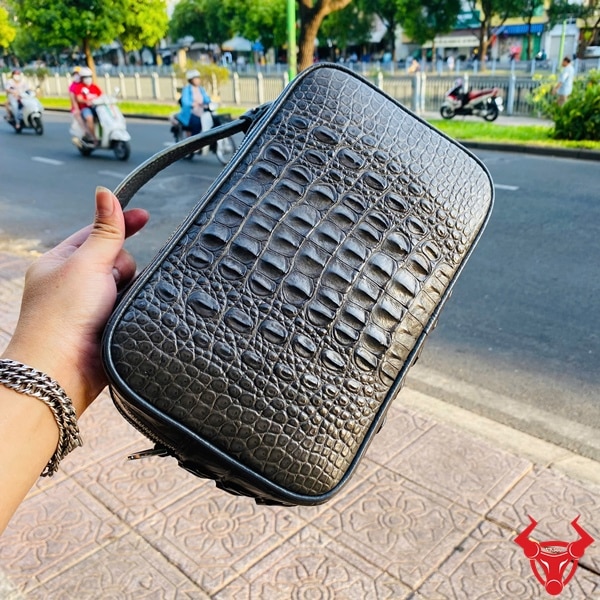 Túi da cá sấu gù xám đậm được cầm tay giữa phố đông xe.