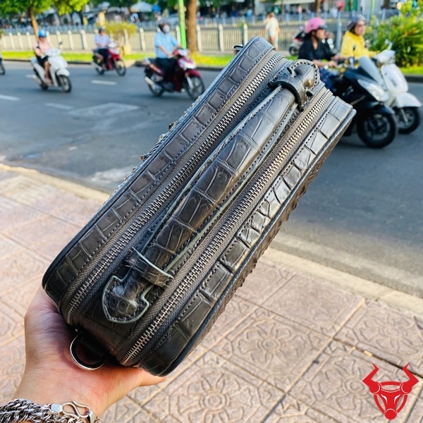 Cận cảnh túi xách tay golf da cá sấu màu xám đậm, vân gồ ghề.