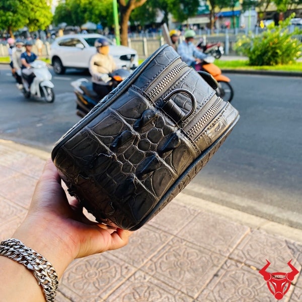 Túi xách tay da cá sấu thật màu xám gù trên nền vỉa hè thành phố.