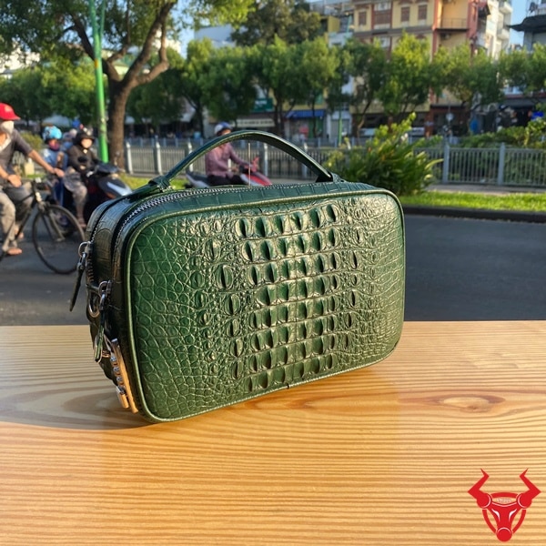 Túi golf da cá sấu xanh lá CJA4 với vân gù nổi bật giữa khung cảnh thành phố.