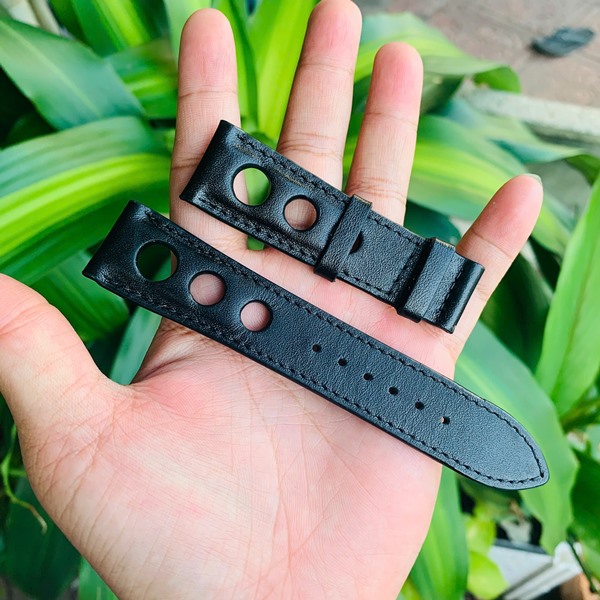 Dây đồng hồ da bò thẩm mỹ và phong cách Hình ảnh dây đồng hồ da bò đen, thiết kế cá nhân, thẩm mỹ, cầm trên tay với nền cây xanh.