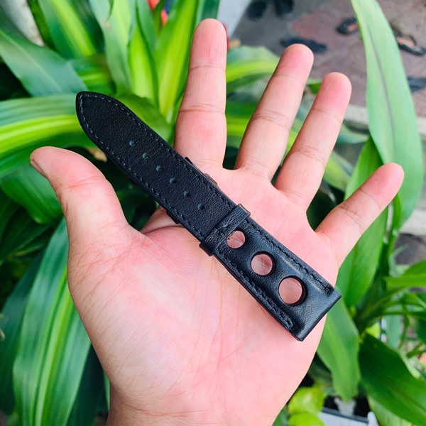 Dây đồng hồ da bò thẩm mỹ tinh tế Hình ảnh dây đồng hồ da bò đen, thiết kế riêng, thẩm mỹ, cầm trên tay với cây xanh.