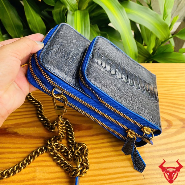 Túi TOD09 - Tiện Ích Và Thời Trang Đẳng Cấp Hình ảnh túi đeo chéo da đà điểu xanh navy với dây xích vàng, trên bàn gỗ, nền cây xanh, nổi bật sự cao cấp và tiện nghi.