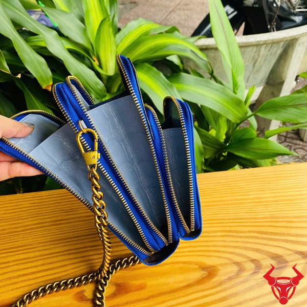 Túi Xanh Navy TOD09 - Thời Trang Mỗi Ngày Hình ảnh túi đeo chéo da đà điểu xanh navy với dây xích vàng, trên bàn gỗ, nền cây xanh, nhấn mạnh sự cao cấp và tiện nghi.