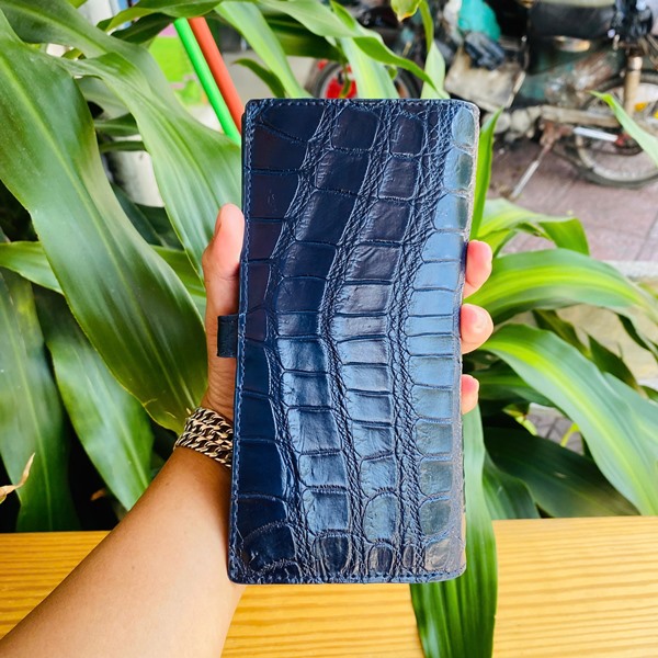 Thời trang cao cấp với ví Thái Lan FBA9B2 Hình ảnh ví da cá sấu Thái Lan hai gấp, xanh đậm, khóa kim loại, cao cấp, trên bàn gỗ với cây xanh.