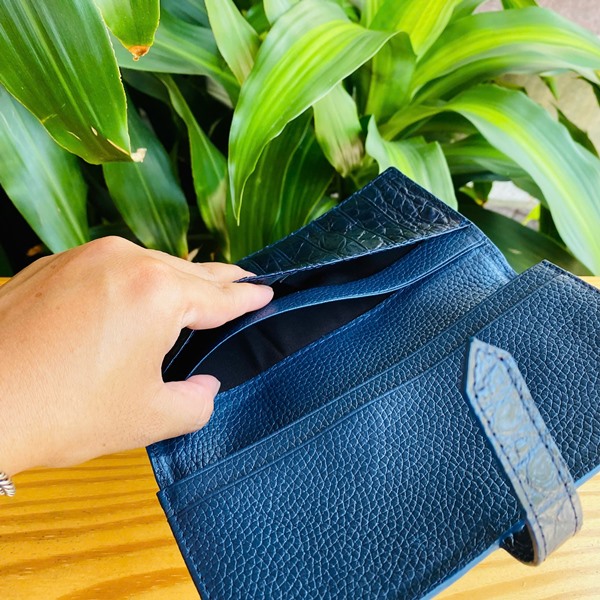 Ví da Thái Lan FBA9B2 - cao cấp cho người thành đạt Hình ảnh ví da cá sấu Thái Lan FBA9B2, xanh đậm, khóa kim loại, quý phái, trên bàn gỗ với cây xanh.