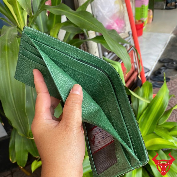 Ví VBA4 Xanh Lá Cao Cấp Và Sang Trọng Độc Đáo Ví nam VBA4 da cá sấu gù lớn xanh lá, tay cầm, nền cây xanh và xe máy.