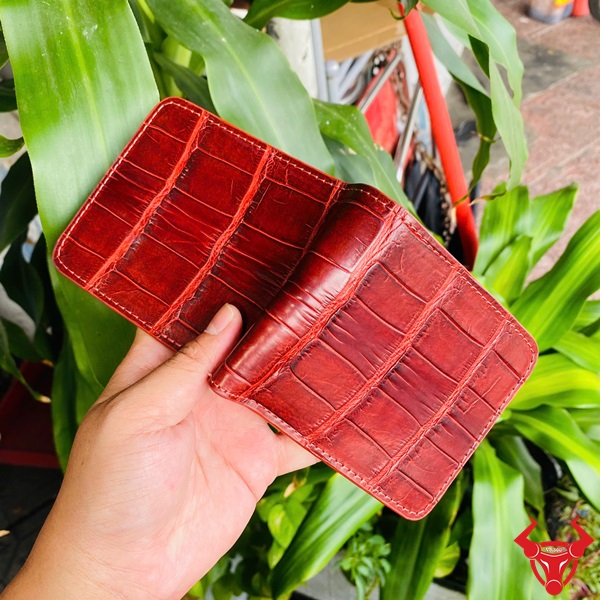 Ví Ngang Da Cá Sấu Nâu Đỏ VBA8 Thời Trang Cao Cấp Độc Đáo Ví ngang da cá sấu màu nâu đỏ VBA8, tay cầm, nền lá xanh và xe máy.