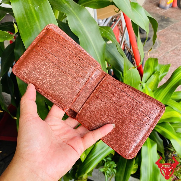 Ví VBA8 Nâu Đỏ Cao Cấp Với Phong Cách Thời Trang Ví ngang da cá sấu màu nâu đỏ VBA8, tay cầm, nền cây xanh và xe máy.