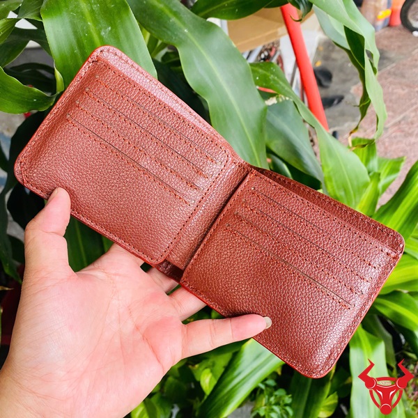 Ví Da Cá Sấu Phối Màu Độc Lạ Và Thời Thượng Ví ngang da cá sấu phối màu trắng-nâu, tay cầm, nền cây xanh và xe máy.