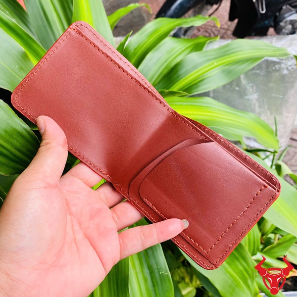 Ví sen cao cấp VUAA8 – Sự lựa chọn cho người thành đạt Ví da cá sấu nâu đỏ cao cấp được chụp ngoài trời nền lá xanh.