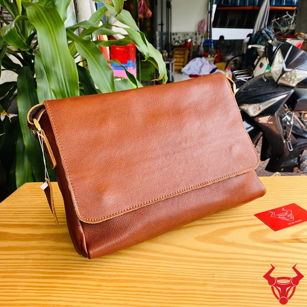 Nâng Tầm Phong Cách Với Túi TN06 Da Bò Hình ảnh túi đeo chéo da bò TN06 màu nâu, form ngang, đặt trên bàn gỗ, nổi bật với phong cách thời trang năng động.