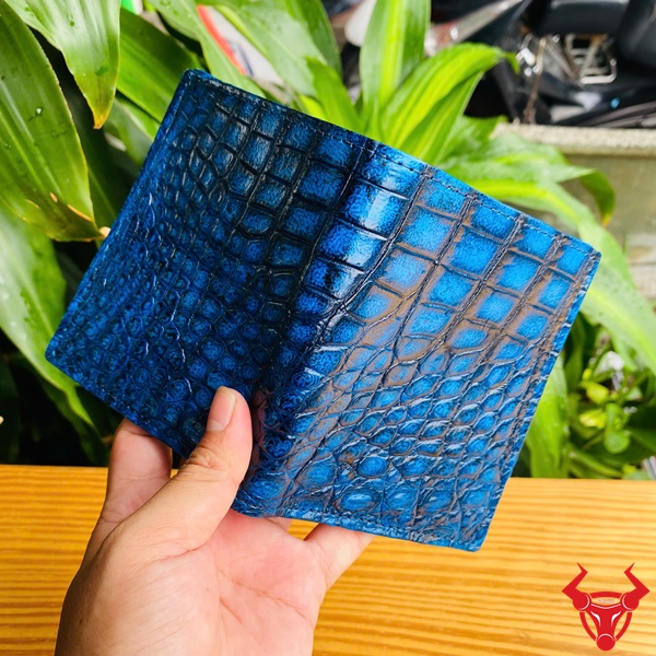 Ví Nam Đứng Da Cá Sấu – Sang Trọng Và Cá Tính Cận cảnh ví đứng da cá sấu màu xanh trên nền cây xanh.