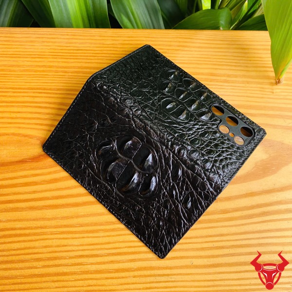 Phụ Kiện Sang Trọng Chắc Chắn Cao Cấp Bền Bỉ Đẳng Cấp Ốp Da Cá Sấu S24 Ultra Gù Lưng Đen Ảnh bao da S24 Ultra da cá sấu gù lưng đen, cầm nghiêng với nền lá, nhấn mạnh sự sang trọng.