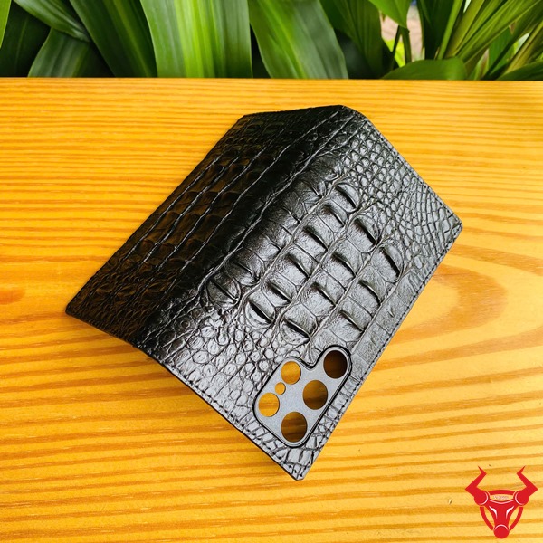 Phụ Kiện Cao Cấp Bền Bỉ Chắc Chắn Sang Trọng Đẳng Cấp Bao Bảo Vệ S24 Ultra Da Gai Cá Sấu Đen Hình ảnh bao da S24 Ultra da cá sấu đen, cầm trên tay trước lá cây, thể hiện sự cao cấp và chắc chắn.