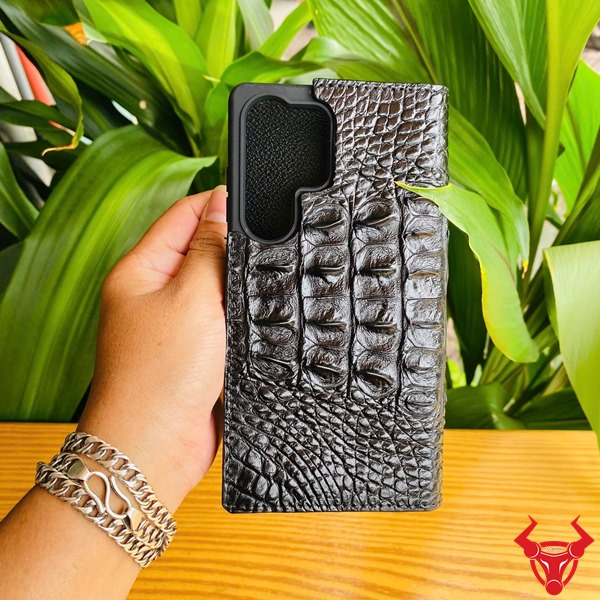 Phụ Kiện Cao Cấp Sang Trọng Bền Bỉ Chắc Chắn Cho Bao Da Samsung S25 Ultra Da Cá Sấu Đen Hình ảnh bao da điện thoại Samsung S25 Ultra da gai lưng cá sấu màu đen, cầm trên tay với nền lá xanh, thể hiện sự cao cấp và chắc chắn.