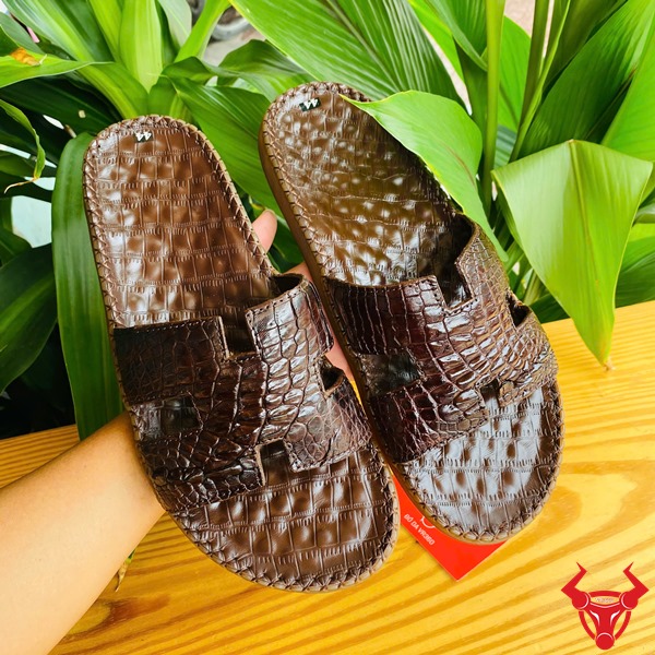 Dép Chữ H Da Cá Sấu Đế Cao Su Cao Cấp Êm Ái Thời Trang Thoải Mái Dep Chu H Da Gai Tay Ca Sau aẢnh dép chữ H da gai tay cá sấu đế cao su, cầm tay với nền lá, nhấn mạnh sự cao cấp và êm chân.De Cao Su 3