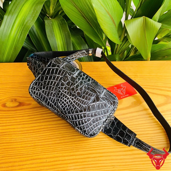Túi Đeo Bụng TTL06 Cá Sấu Đen Đa Dụng Năng Động Thời Trang Hình ảnh túi đeo bụng TTL06 da cá sấu đen, trên bàn gỗ với nền lá, thể hiện sự đa dụng và hiện đại.