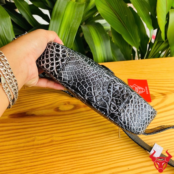 Túi Đeo Bụng TTL06 Da Cá Sấu Đen Thời Trang Đa Dụng Năng Động Hình túi đeo bụng TTL06 da cá sấu đen, trên bàn gỗ với nền lá, thể hiện sự thời trang.