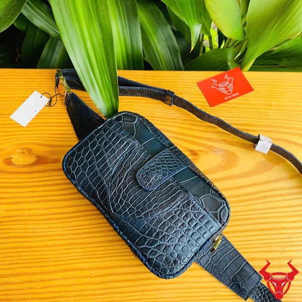 Túi Đeo Bụng TTL06 Da Cá Sấu Xanh Navy Đa Dụng Thời Trang Năng Động Hình túi đeo bụng TTL06 da cá sấu xanh navy, trên bàn gỗ với nền lá, thể hiện sự đa dụng và thời trang.