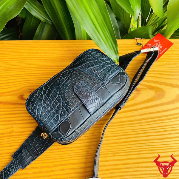 Túi Đeo Bụng TTL06 Cá Sấu Xanh Navy Đa Dụng Năng Động Thời Trang Hình ảnh túi đeo bụng TTL06 da cá sấu xanh navy, trên bàn gỗ với nền lá, thể hiện sự đa dụng và hiện đại.