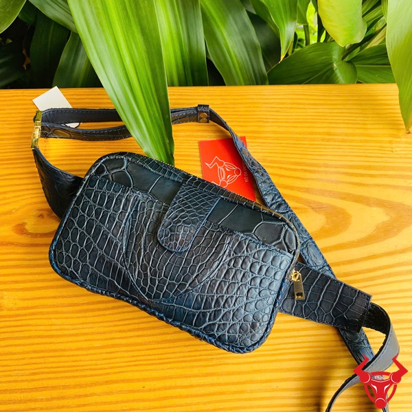 Túi Đeo Bụng TTL06 Da Cá Sấu Xanh Navy Thời Trang Đa Dụng Năng Động Hình túi đeo bụng TTL06 da cá sấu xanh navy, trên bàn gỗ với nền lá, thể hiện sự thời trang.