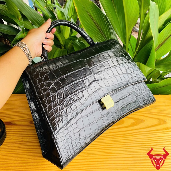 Túi Xách Da Cá Sấu TTL07 Đen Cao Cấp Thời Trang Quý Phái Đẳng Cấp Hình túi xách TTL07 da cá sấu đen size lớn, đặt trên bàn gỗ với lá xanh, thể hiện sự cao cấp.