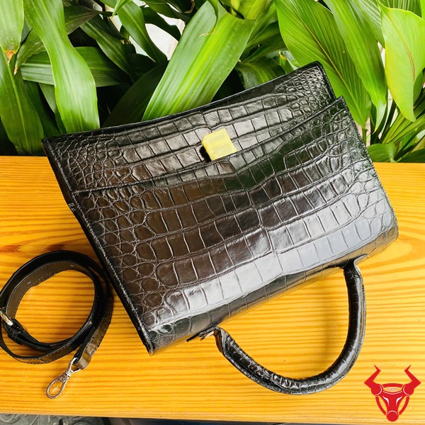 Túi Xách TTL07 Da Cá Sấu Đen Cao Cấp Quý Phái Thời Trang Đẳng Cấp Ảnh túi xách TTL07 da cá sấu đen size lớn, đặt trên bàn với nền lá, nhấn mạnh sự cao cấp.