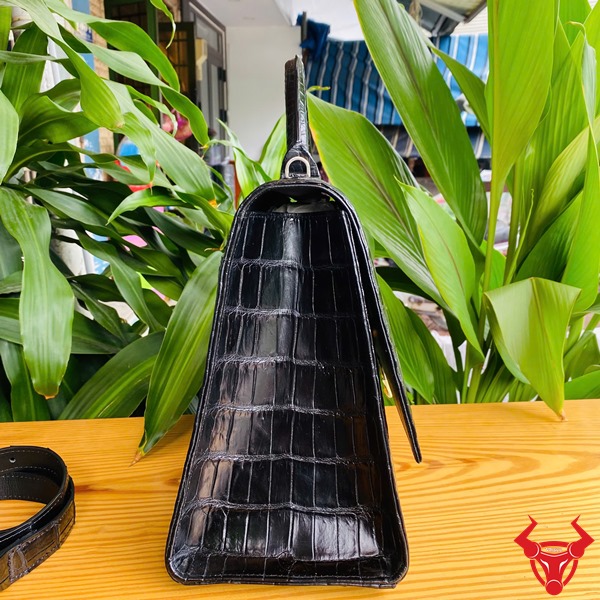 Túi Xách Nữ TTL07 Cá Sấu Đen Đẳng Cấp Thời Trang Cao Cấp Quý Phái Hình túi xách TTL07 da cá sấu đen size lớn, trên bàn gỗ với lá xanh, thể hiện sự đẳng cấp.