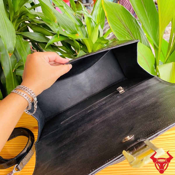 Túi Xách Da Cá Sấu TTL07 Đen Quý Phái Cao Cấp Thời Trang Đẳng Cấp Ảnh túi xách TTL07 da cá sấu đen size lớn, đặt trên bàn với nền lá, nhấn mạnh sự quý phái.