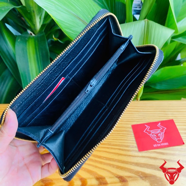 Đẳng Cấp Cao Cấp: Ví Cầm Tay Da Cá Sấu BUA4 Đen Sang Trọng Bền Bỉ Thời Trang Ảnh người cầm ví da cá sấu đen cao cấp, nền lá xanh, thẻ thương hiệu bên cạnh.