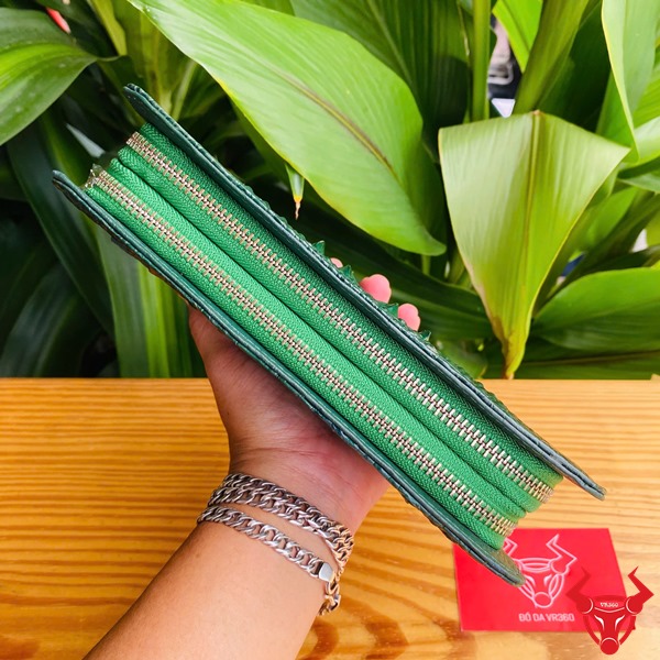 Cao Cấp Đẳng Cấp: Ví Da Cá Sấu Gù BIA4 Xanh Lá Thời Trang Sang Trọng Tiện Dụng Ảnh ví da cá sấu xanh lá cao cấp cầm tay, nền lá xanh, kèm thẻ thương hiệu đỏ.