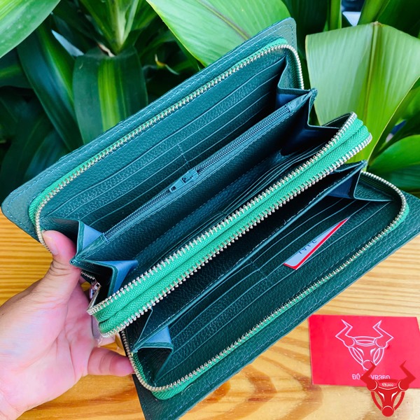 Sang Trọng Thời Trang: Ví Nam Nữ BIA4 Xanh Lá Đẳng Cấp Cao Cấp Tiện Dụng Hình ảnh ví da cá sấu xanh lá cầm tay, nền lá xanh, thẻ thương hiệu đỏ bên cạnh.
